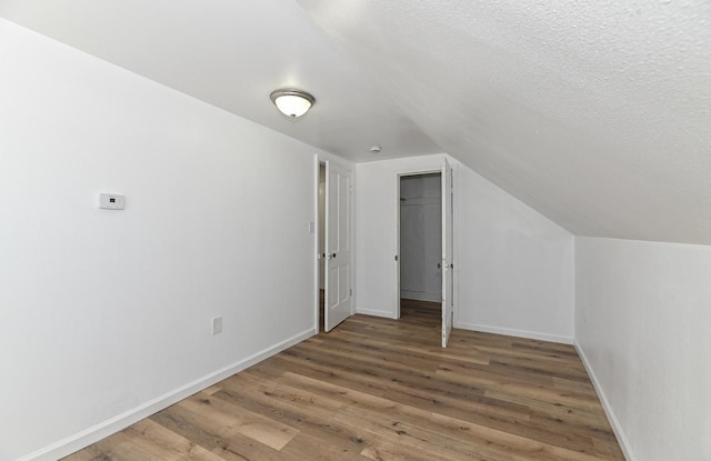 bonus room featuring vaulted ceiling, a textured ceiling, baseboards, and wood finished floors