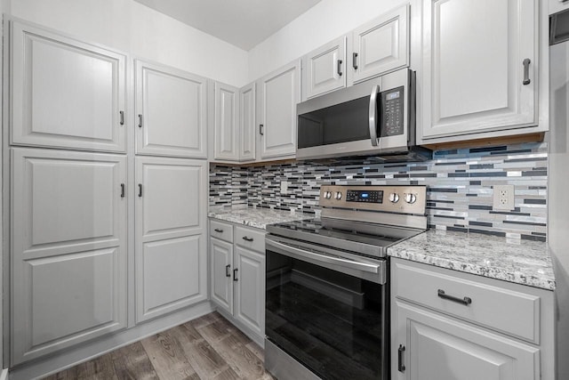 kitchen featuring light stone counters, backsplash, light wood-type flooring, and appliances with stainless steel finishes