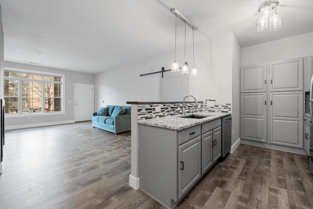 kitchen with gray cabinets, a sink, stainless steel dishwasher, open floor plan, and dark wood-style flooring
