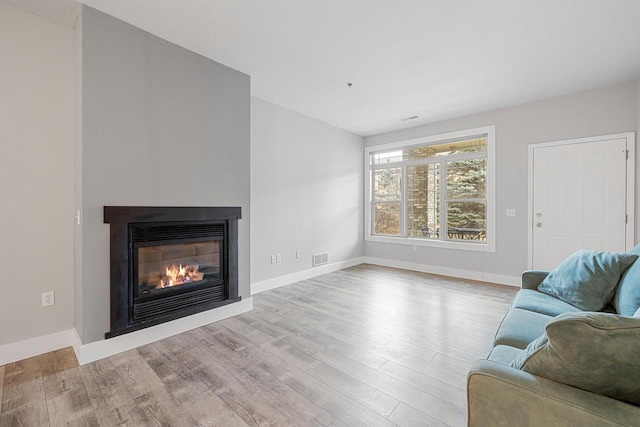 living room featuring a glass covered fireplace, baseboards, and wood finished floors