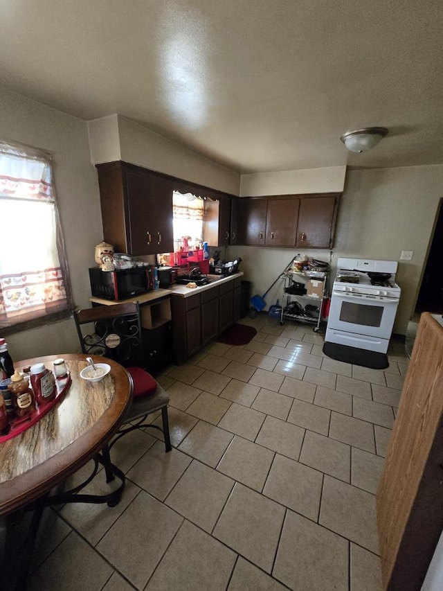 kitchen featuring light tile patterned floors, dark brown cabinetry, light countertops, white gas range oven, and black microwave