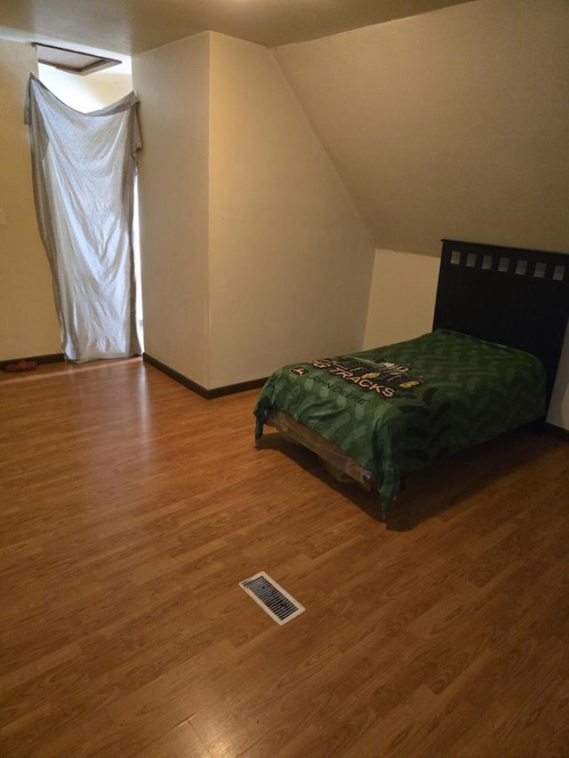 bedroom with visible vents, lofted ceiling, baseboards, and wood finished floors