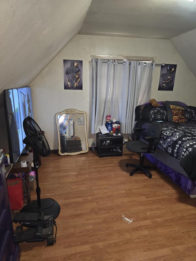 bedroom with vaulted ceiling, wood finished floors, and a textured ceiling
