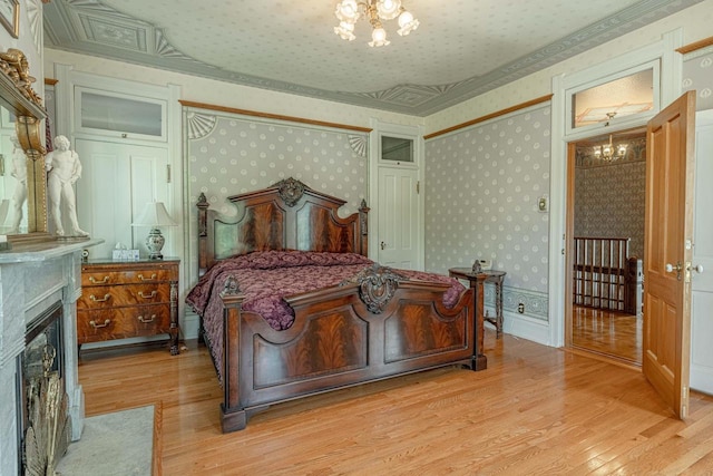 1222 11th St, Monroe, WI 53566 - bedroom with a chandelier, light wood-type flooring, wallpapered walls, a fireplace with flush hearth, and ornamental molding