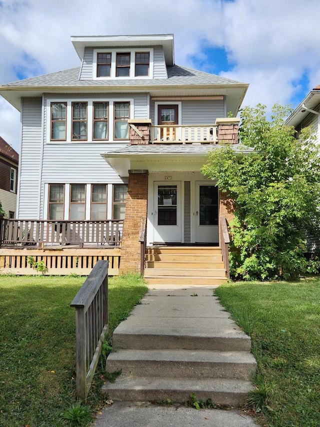 american foursquare style home with a front lawn, a balcony, covered porch, and roof with shingles
