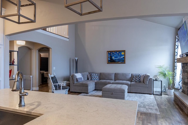 living room featuring wood finished floors, arched walkways, a towering ceiling, and a fireplace with raised hearth