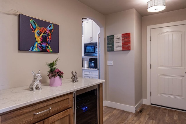 bar with beverage cooler, built in microwave, wood finished floors, arched walkways, and baseboards