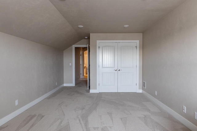 unfurnished bedroom featuring carpet flooring, vaulted ceiling, a closet, and baseboards