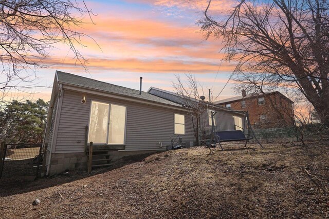 back of house at dusk featuring entry steps and fence