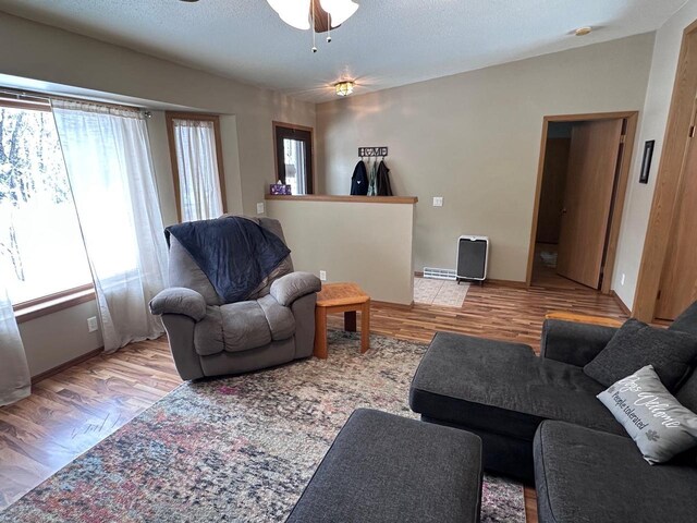 living area featuring a textured ceiling, baseboards, ceiling fan, and wood finished floors