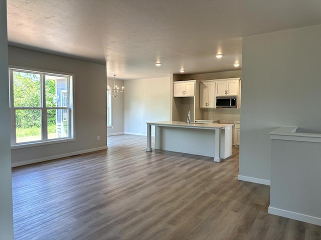 N9249 Constellation Dr, Appleton, WI 54915 - kitchen featuring stainless steel microwave, a chandelier, white cabinetry, dark wood-type flooring, and an island with sink