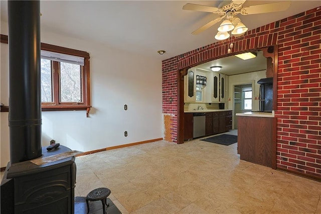 kitchen featuring a wood stove, baseboards, dishwasher, a ceiling fan, and light floors