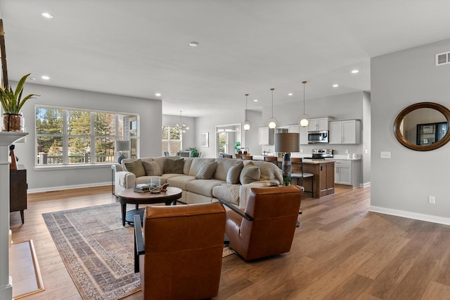 living area with visible vents, baseboards, recessed lighting, light wood-type flooring, and a notable chandelier