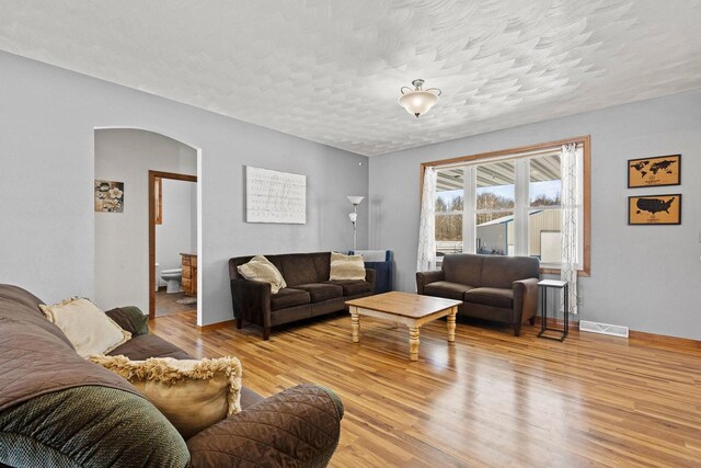 8464 County Rd S, Pulaski, WI 54162 - living room featuring a textured ceiling, visible vents, baseboards, arched walkways, and light wood-style floors