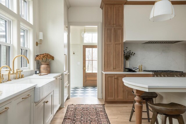 545 Wisconsin Ave, Delafield, WI 53018 - kitchen with light countertops, a kitchen bar, light wood-type flooring, backsplash, and ventilation hood