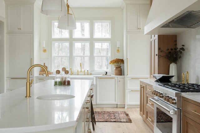 545 Wisconsin Ave, Delafield, WI 53018 - kitchen with high end stainless steel range, light countertops, white cabinetry, light wood-style flooring, and under cabinet range hood