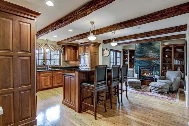 3736 Forest Knoll Dr, Eau Claire, WI 54701 - kitchen featuring a kitchen breakfast bar, decorative light fixtures, a large fireplace, light wood finished floors, and brown cabinets