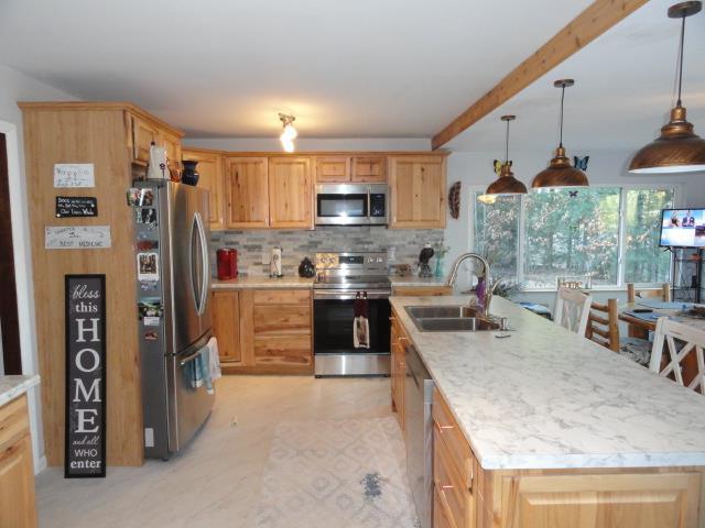 kitchen featuring stainless steel appliances, decorative backsplash, a sink, beam ceiling, and a kitchen island with sink