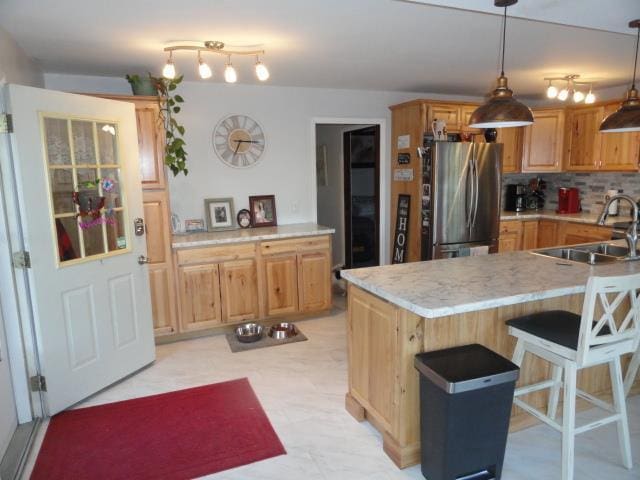 kitchen with light countertops, a sink, a breakfast bar area, backsplash, and freestanding refrigerator