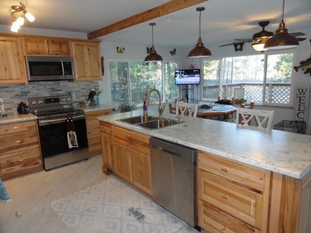 kitchen with a sink, backsplash, appliances with stainless steel finishes, light brown cabinets, and ceiling fan