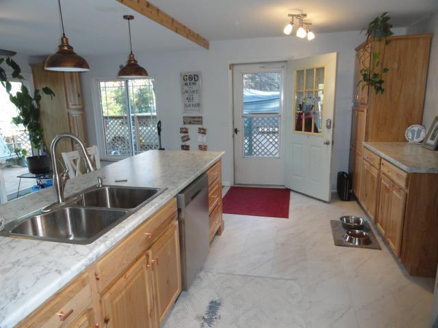 kitchen featuring light countertops, beam ceiling, a sink, hanging light fixtures, and stainless steel dishwasher