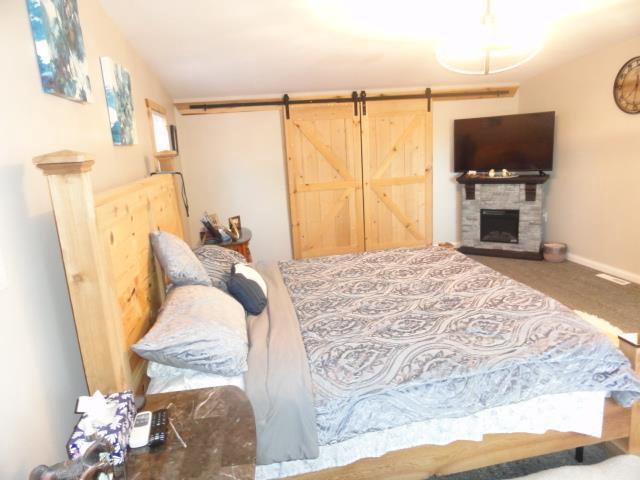 bedroom featuring a stone fireplace, carpet, a barn door, and baseboards