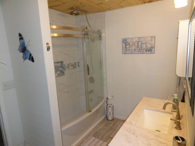 full bath with bath / shower combo with glass door, baseboards, wood finished floors, vanity, and wood ceiling