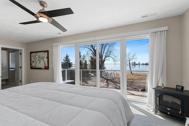 bedroom with carpet flooring, a water view, visible vents, ceiling fan, and a wood stove