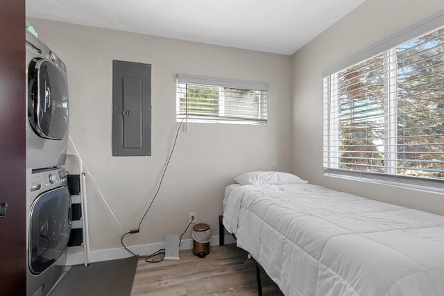 bedroom with baseboards, stacked washer / drying machine, electric panel, and wood finished floors