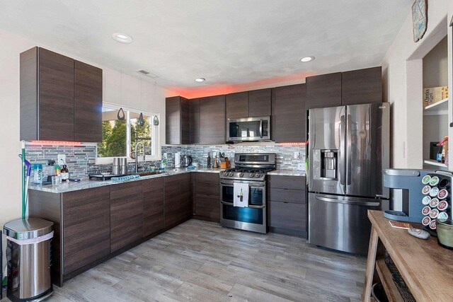 kitchen featuring backsplash, light wood finished floors, stainless steel appliances, visible vents, and dark brown cabinets