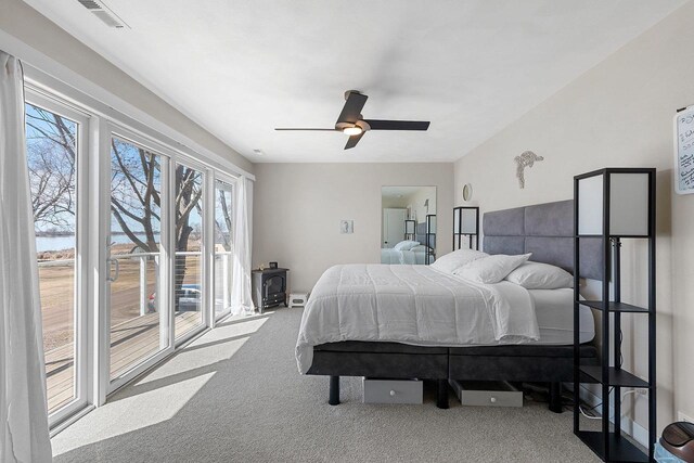 bedroom with a wood stove, carpet, access to outside, visible vents, and a ceiling fan