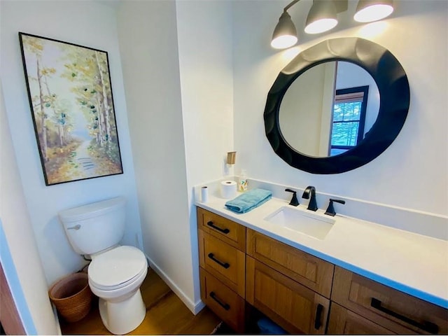 half bathroom featuring baseboards, toilet, vanity, and wood finished floors