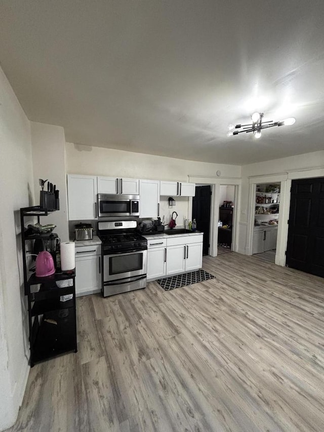 kitchen with light wood finished floors, white cabinetry, a sink, and stainless steel appliances