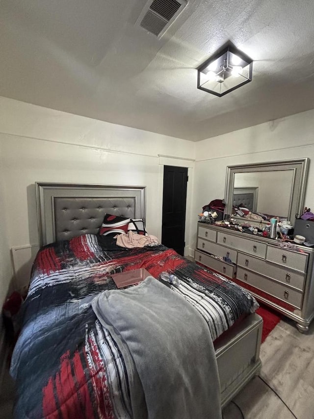 bedroom featuring a textured ceiling, visible vents, and wood finished floors