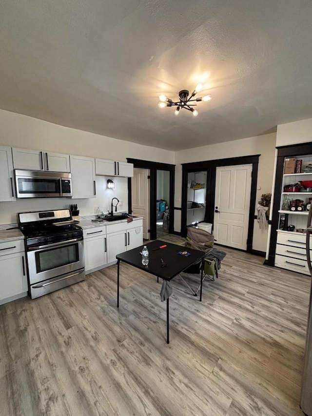 kitchen featuring light wood-style flooring, appliances with stainless steel finishes, white cabinetry, a sink, and an inviting chandelier