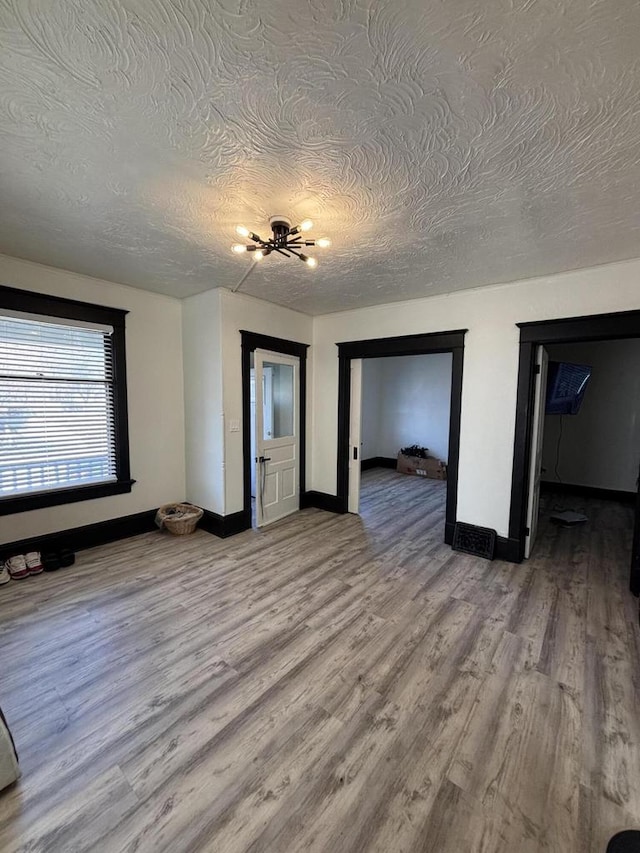 unfurnished bedroom featuring a notable chandelier, baseboards, light wood finished floors, and a textured ceiling
