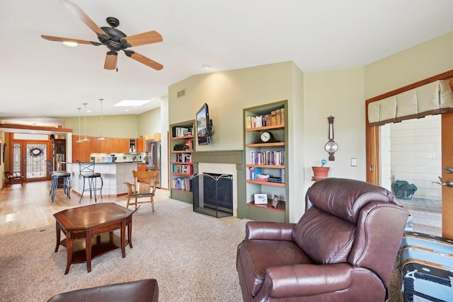 living area with lofted ceiling, light colored carpet, a fireplace with flush hearth, visible vents, and a ceiling fan