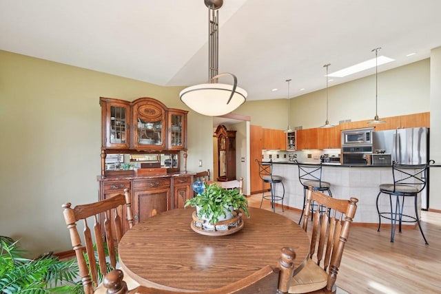 dining space with high vaulted ceiling, a skylight, and light wood finished floors