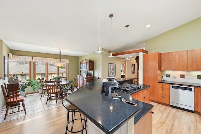 kitchen with light wood-style flooring, dishwasher, a breakfast bar, an island with sink, and pendant lighting