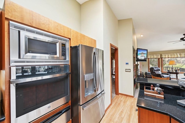 kitchen with a ceiling fan, open floor plan, light wood-style flooring, dark stone countertops, and stainless steel appliances