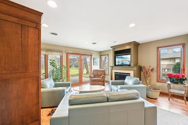 living room with recessed lighting, baseboards, visible vents, light wood-style flooring, and a glass covered fireplace