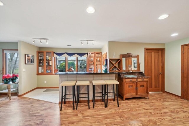 kitchen with a kitchen breakfast bar, recessed lighting, baseboards, light wood-style flooring, and brown cabinets