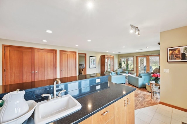kitchen featuring recessed lighting, light tile patterned floors, dark stone countertops, baseboards, and a sink