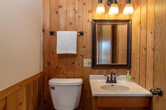 half bath with toilet, vanity, wood walls, and wainscoting