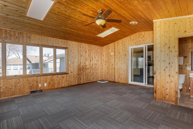empty room featuring lofted ceiling, a ceiling fan, dark carpet, and wooden walls