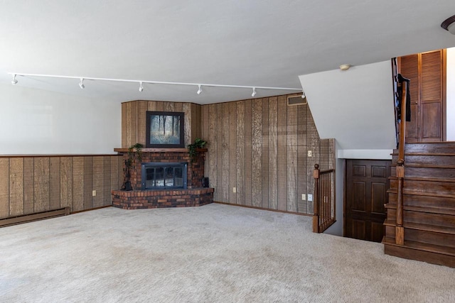 living area featuring track lighting, a fireplace, wooden walls, a baseboard heating unit, and carpet