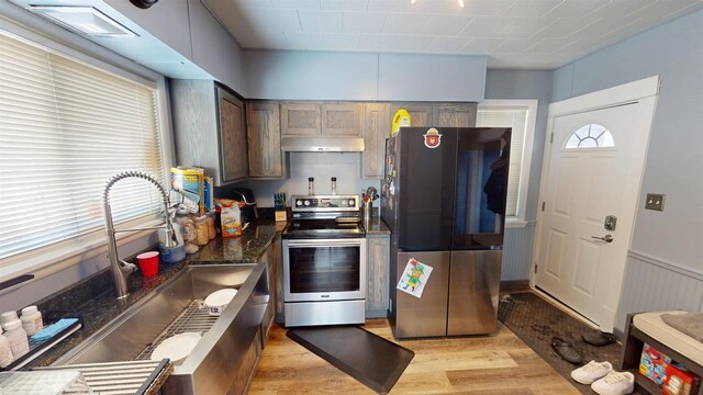 813 Main St, Black River Falls, WI 54615 - kitchen with a sink, wainscoting, light wood-type flooring, under cabinet range hood, and stainless steel appliances