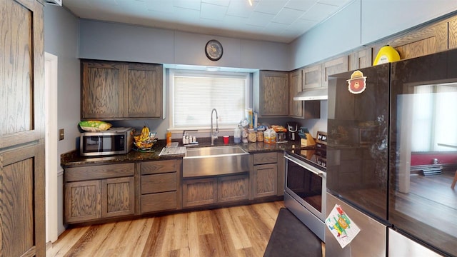 813 Main St, Black River Falls, WI 54615 - kitchen with dark stone counters, stainless steel appliances, under cabinet range hood, a sink, and light wood-style floors