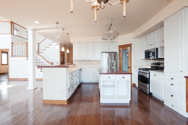 kitchen with white cabinets, a peninsula, dark wood-type flooring, stainless steel appliances, and tasteful backsplash