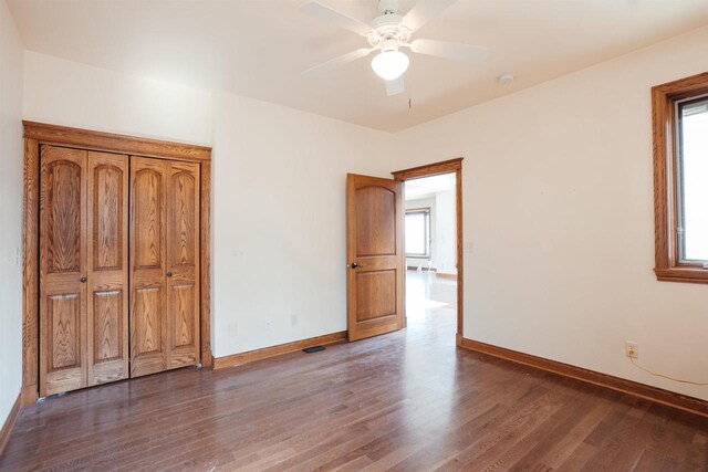 unfurnished bedroom featuring ceiling fan, baseboards, multiple windows, and wood finished floors